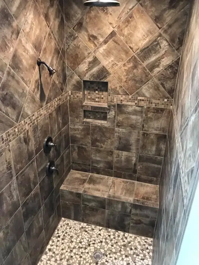 Brown stone-look tile shower with a built-in bench, mosaic accent band and stacked niches
