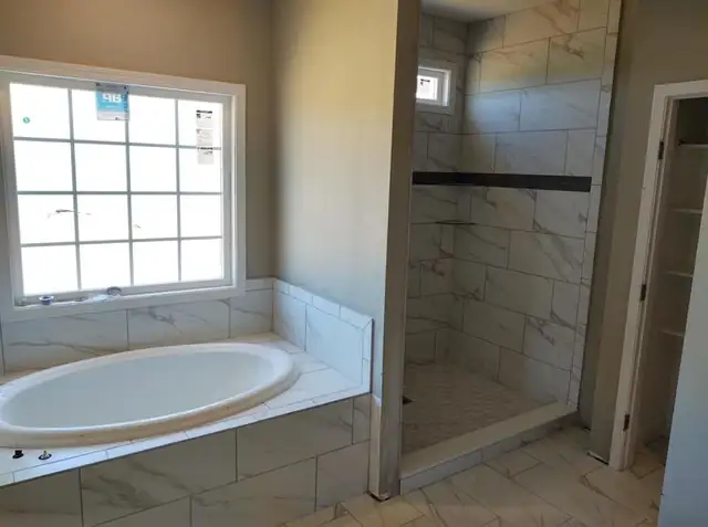 Bathroom with a tiled drop-in tub deck under a large window and a walk-in shower beside it
