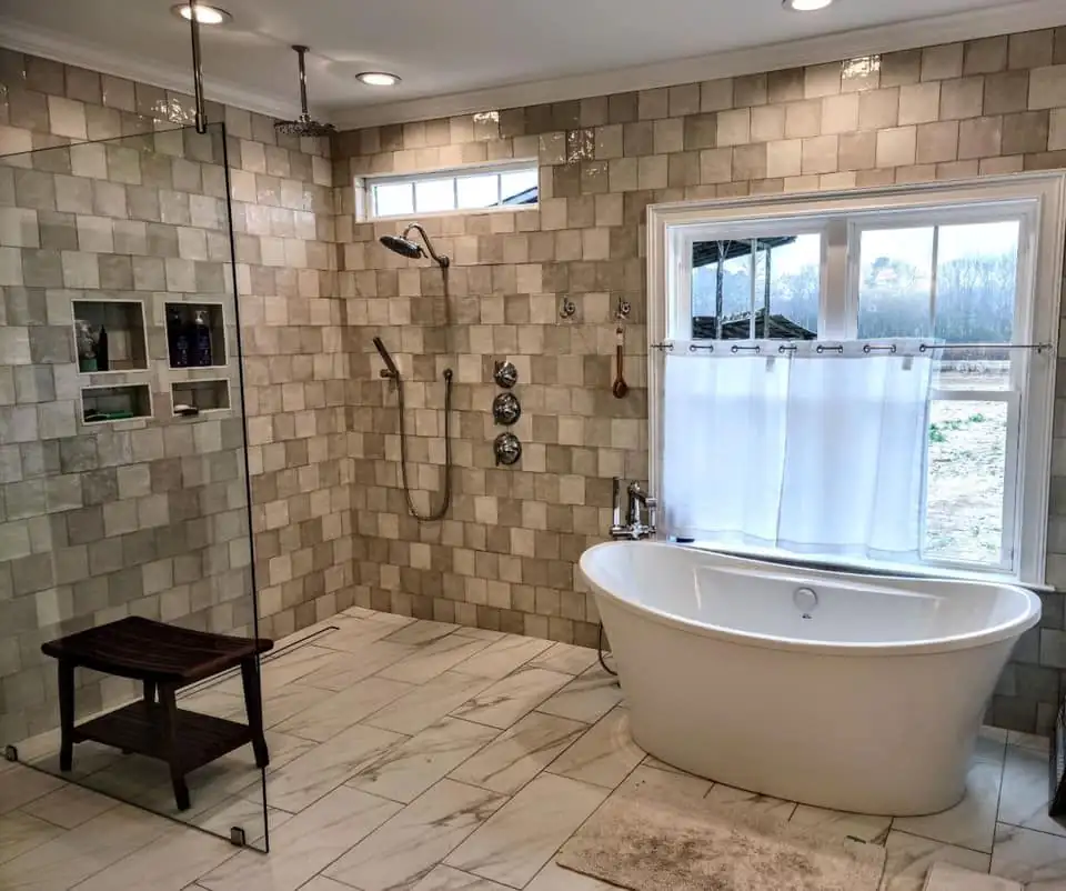 Open tiled shower with built-in niches and a glass panel beside a freestanding tub, posted by Preferred Tile, a tile store in Statesboro, GA