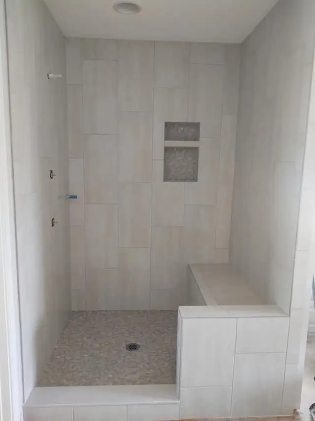 Light tile shower with a mosaic niche and a long tiled bench