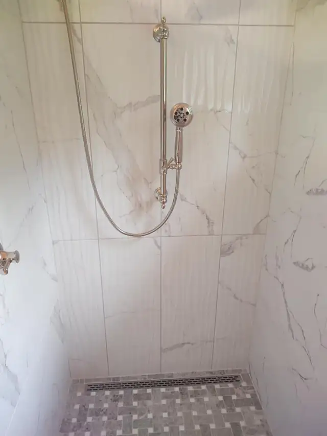 Large-format white marble-look tile on a shower wall with a handheld shower